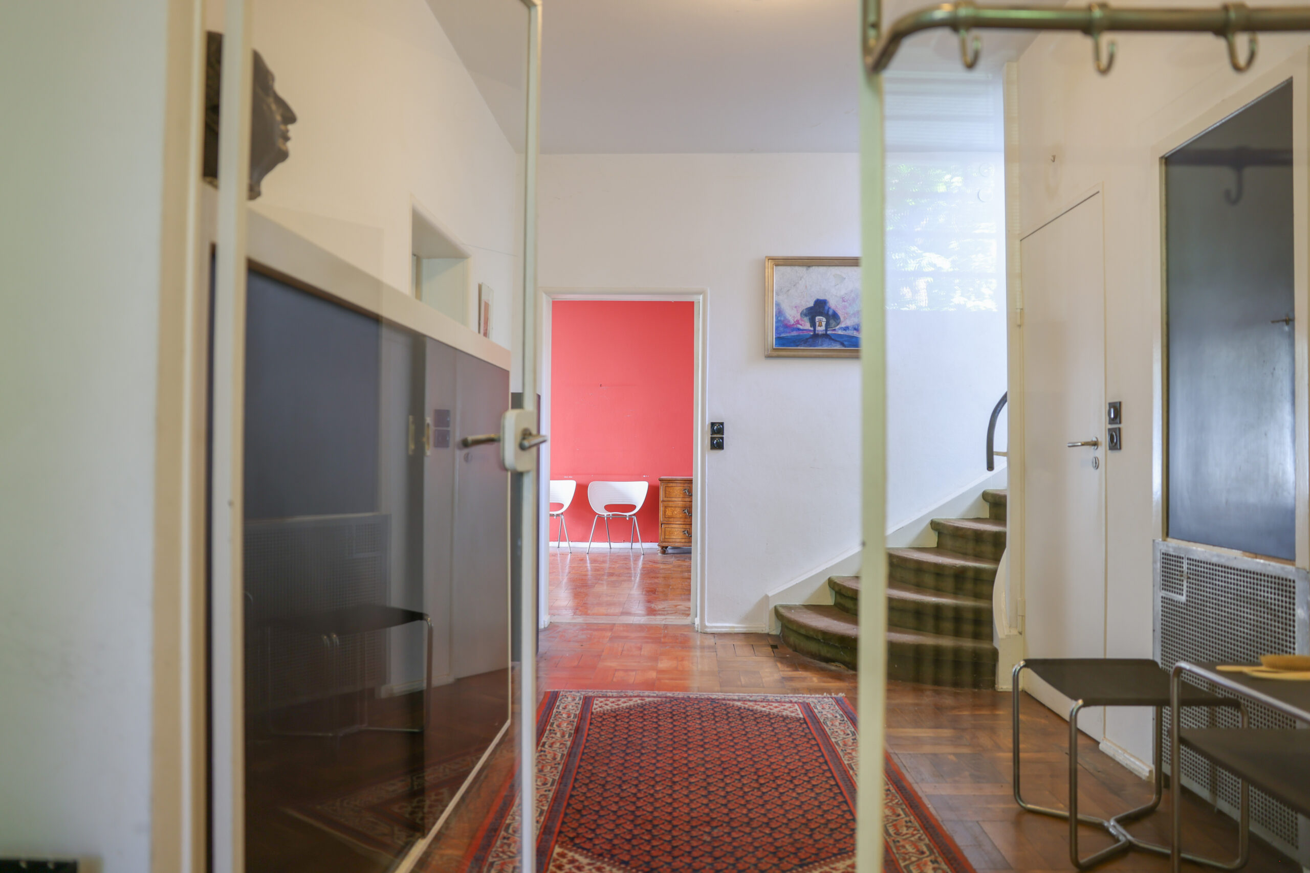 Garderobe mit Glastür als Ganzes, dahinter Diele, Treppe und Wohnraum des Haus Lewin